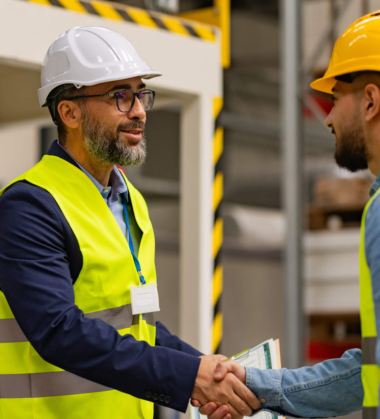Two individuals in safety gear shaking hands in a warehouse setting